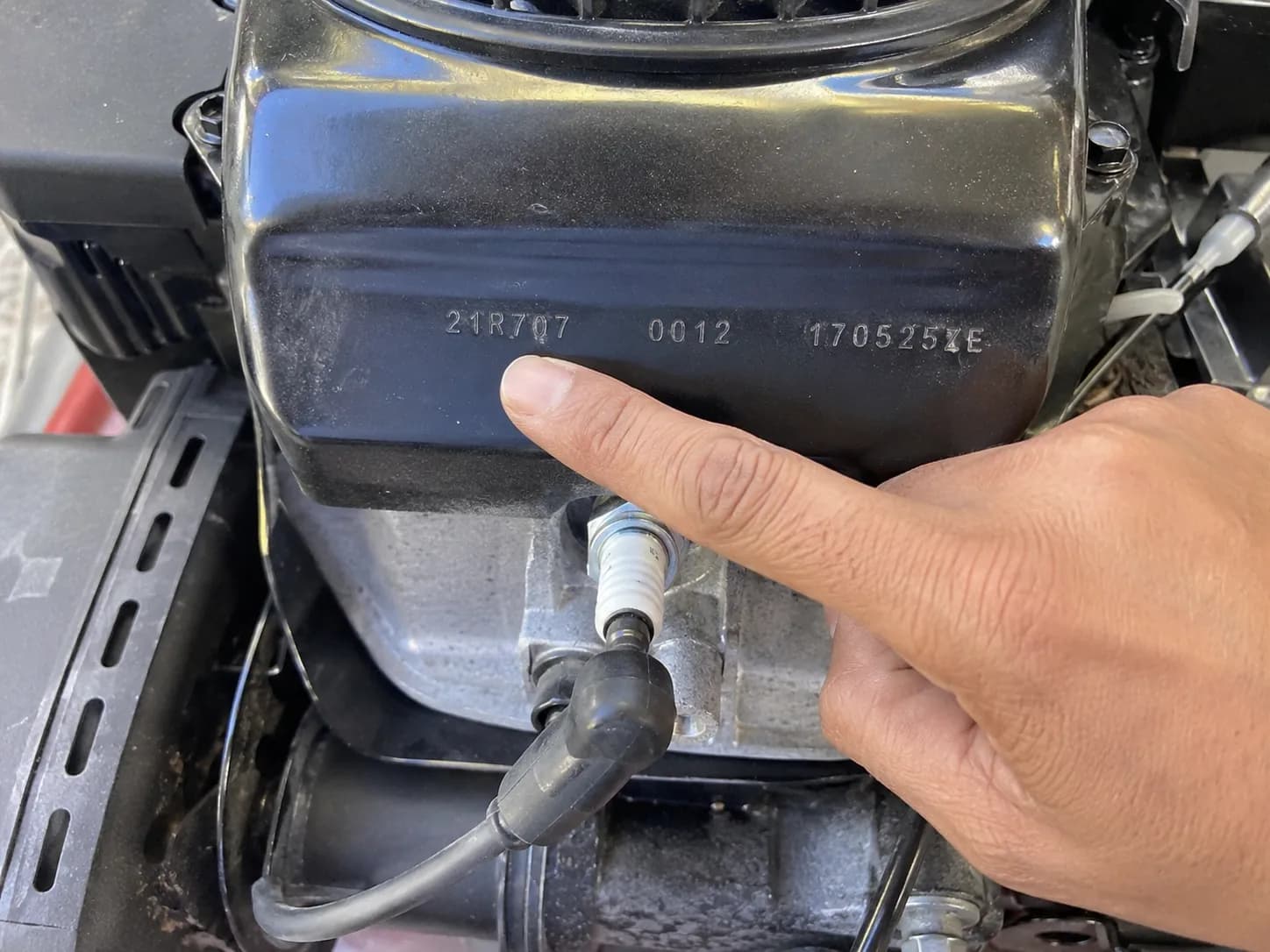 Close-up of a small engine shroud showing stamped model, type, and code numbers above the spark plug, with a finger indicating the first number.
