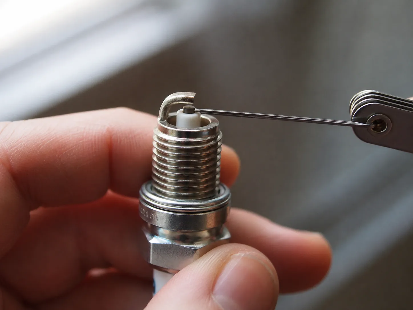 Close-up of a wire feeler gauge measuring the electrode gap on a new lawn mower spark plug before installation.
