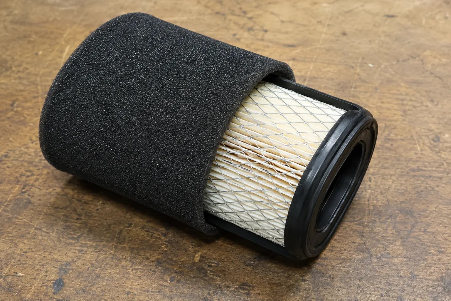 Dual-stage mower air filter with the black foam pre-filter sleeve pulled halfway off the pleated paper core, showing the two separate filter layers on a workbench.