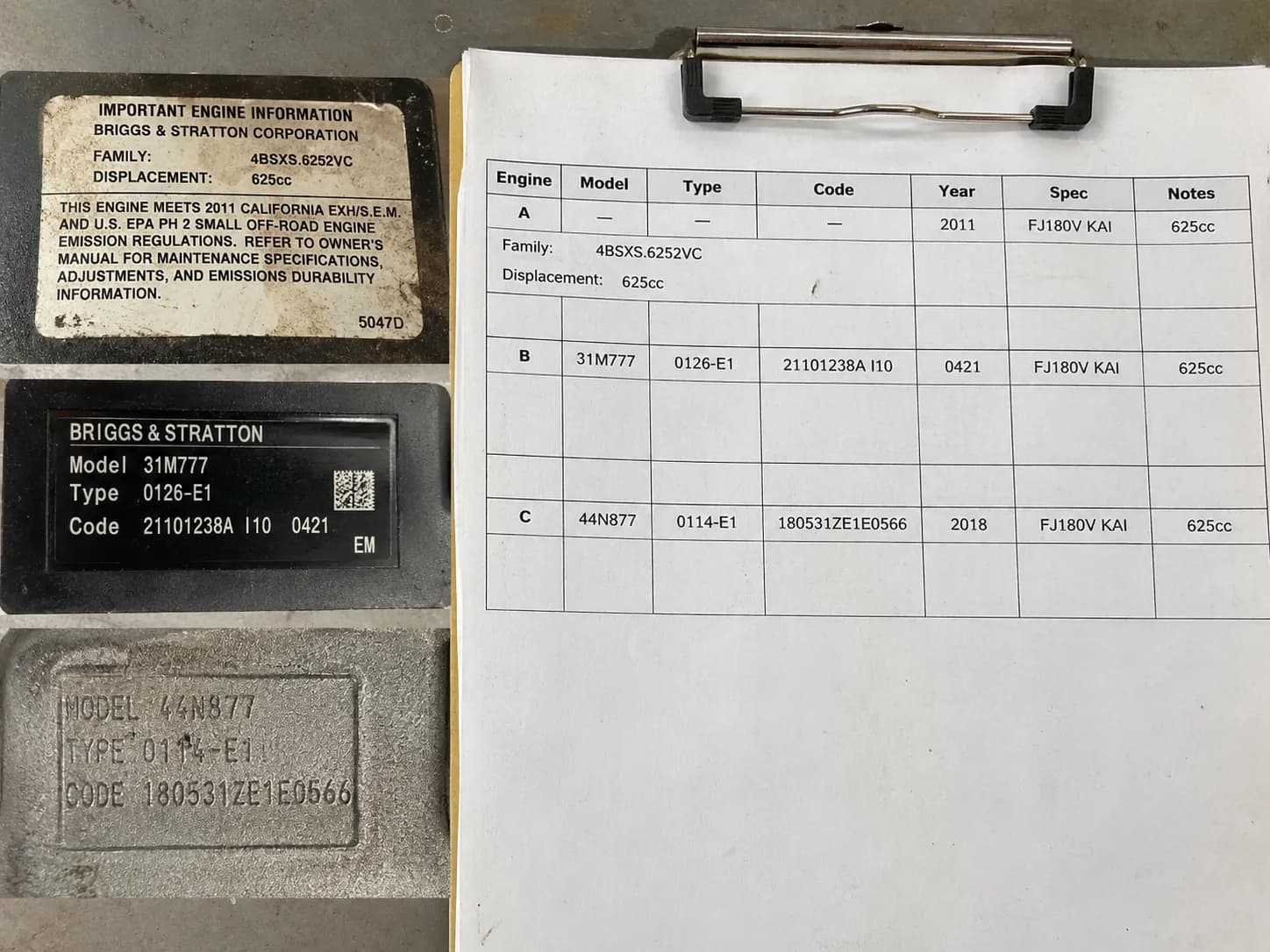 Three engine specification stickers arranged beside a printed engine lookup table on a clipboard for identifying and matching fleet engine specifications.
