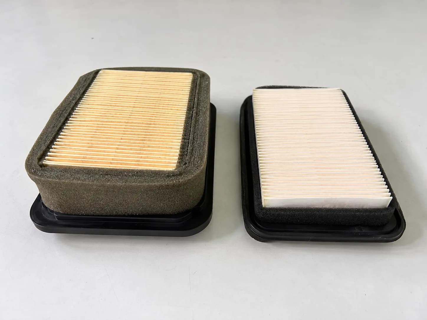 Side-by-side comparison of a genuine-style Honda lawn mower air filter and a budget aftermarket filter, highlighting differences in pleat depth, foam thickness, and overall build quality.