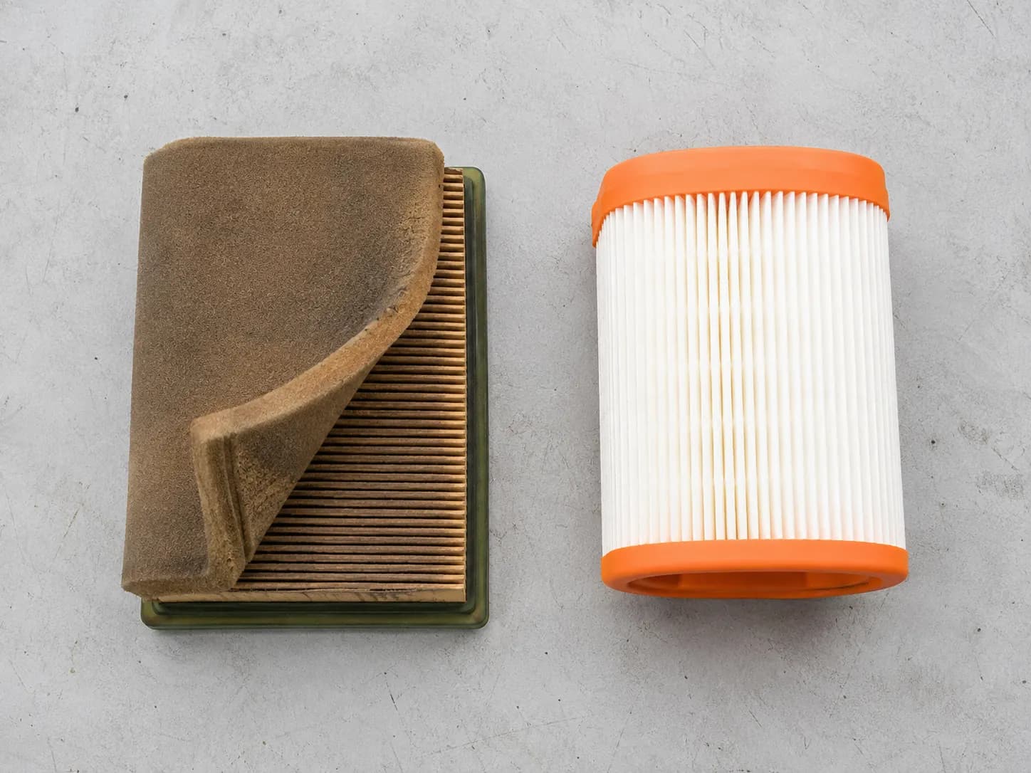 Older Honda foam-wrapped air filter beside a newer white paper air filter with orange trim, showing the two filter generations are different and not interchangeable.