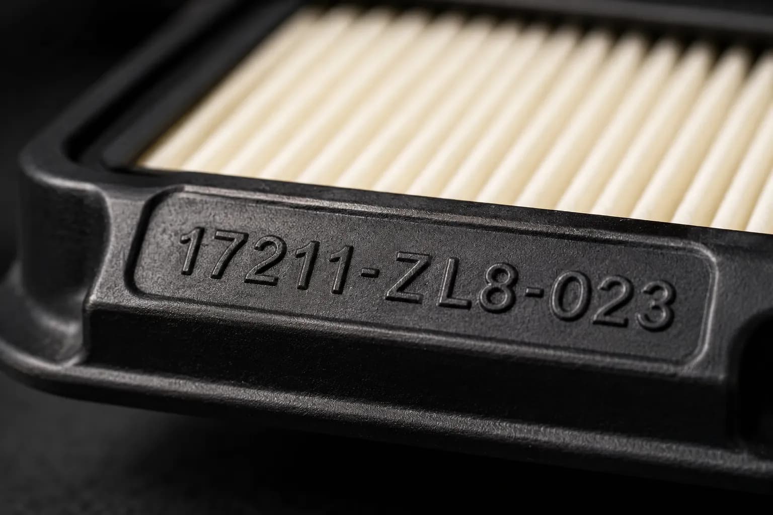 Macro close-up of a Honda lawn mower air filter frame with the molded part number in sharp focus, while the paper filter pleats fade into a soft blur behind.