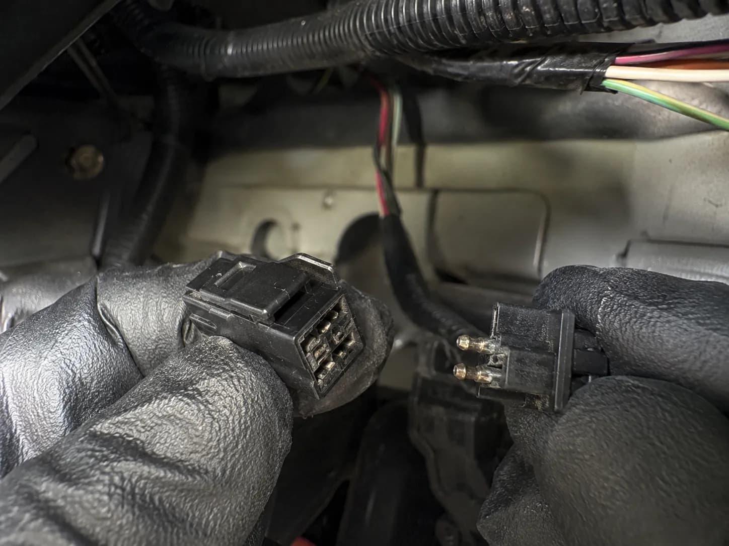 Close-up of a disconnected two-pin electrical connector beneath a lawn tractor dashboard, showing lightly tarnished contacts on the blade interlock wiring harness during troubleshooting.