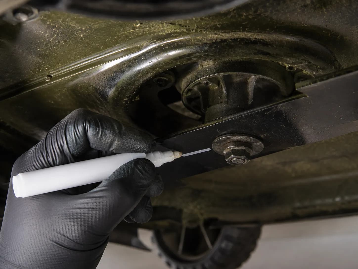 Gloved hand marking the downward-facing side of a lawn mower blade with a paint marker before removing the blade bolt to ensure correct reinstallation.