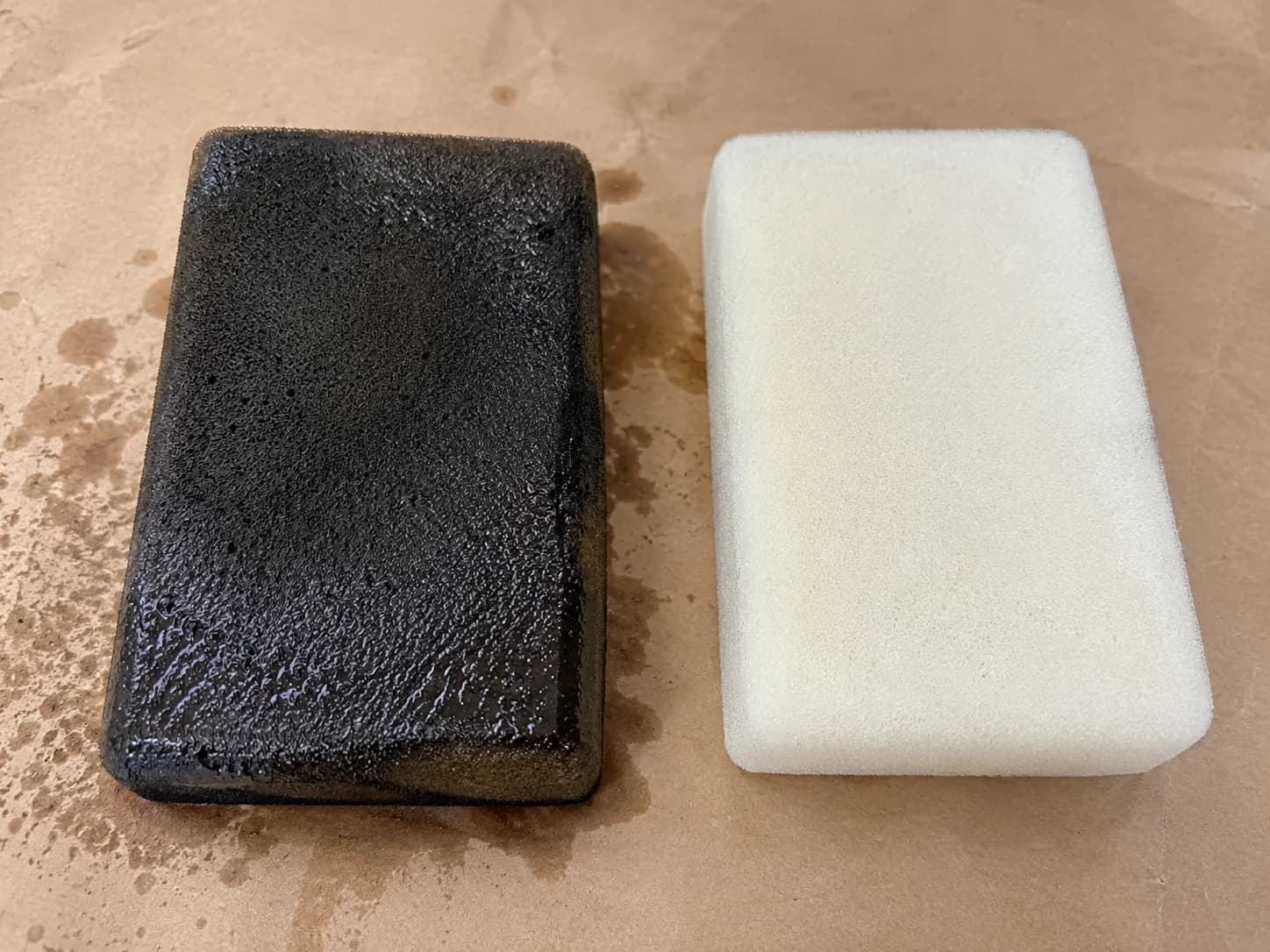 Oil-soaked foam mower pre-cleaner beside a clean foam pre-cleaner on kraft paper, highlighting the difference in color, texture, and oil saturation.