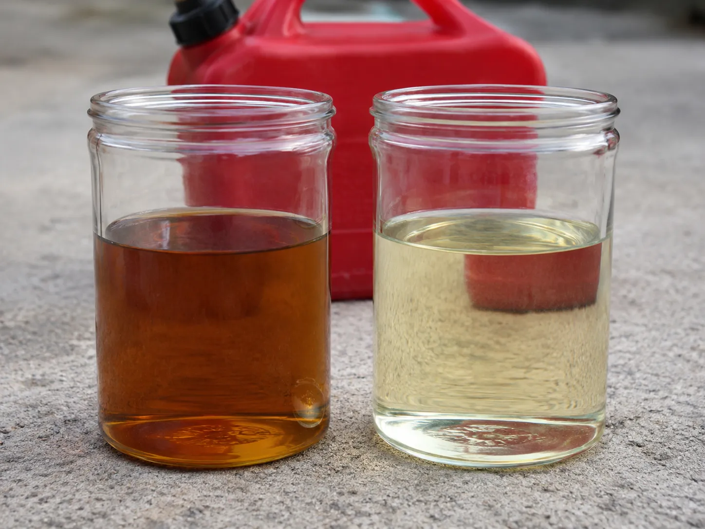 Side-by-side comparison of old drained petrol and fresh gasoline in clear glass jars, showing the darker aged fuel versus clean fresh fuel for lawn mower maintenance.