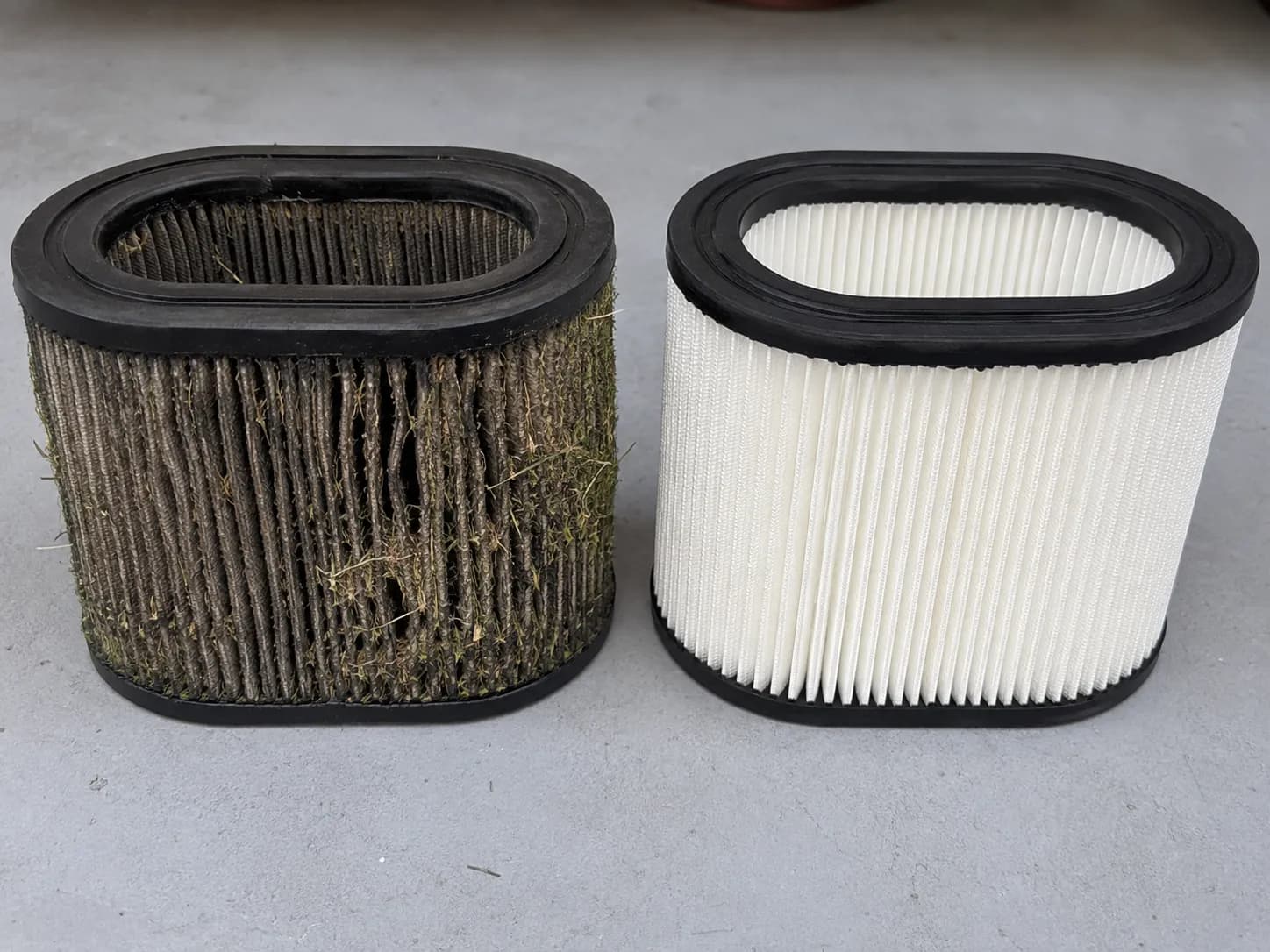 Old grey clogged lawn mower paper air filter beside a clean bright white replacement filter, showing the difference before and after a tune-up.