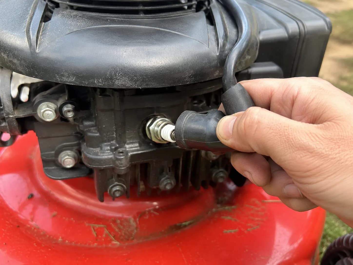 Hand pulling the rubber spark plug boot off a Toro lawn mower engine, with the spark plug location clearly visible before removal.