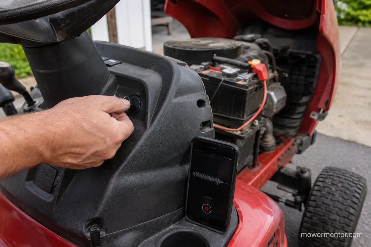 hand turning the ignition key on a riding mower while a phone records the clicking sound