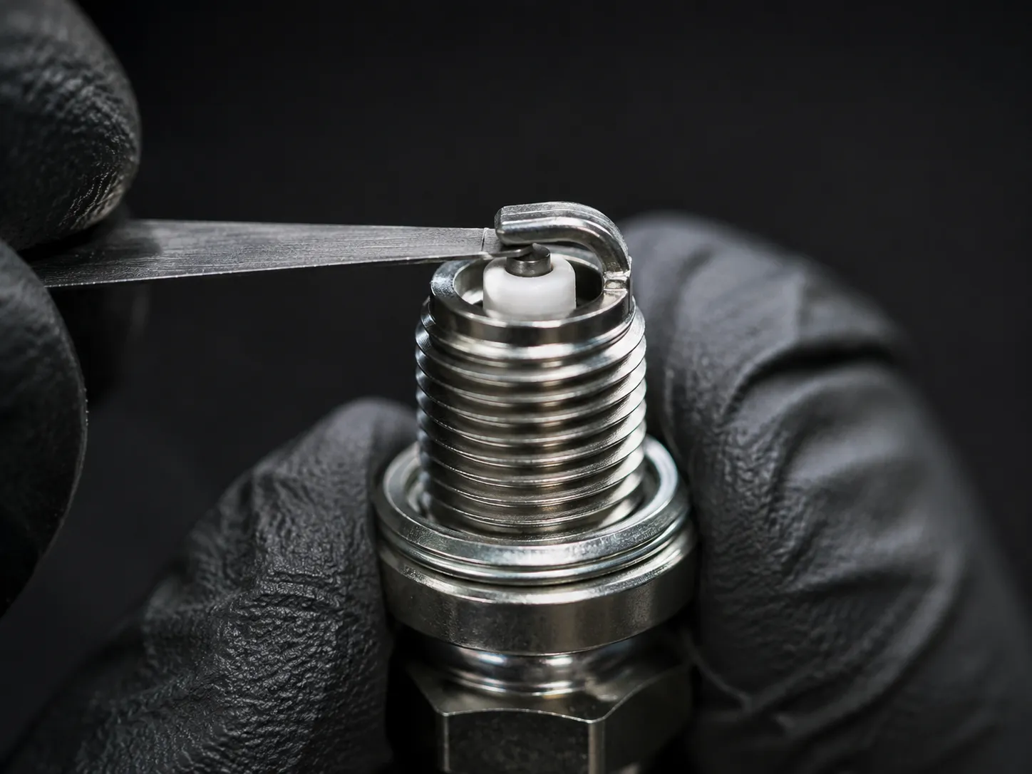Macro close-up of a new small engine spark plug being checked with a steel feeler gauge, showing the electrode gap before installation to verify the correct spark plug gap specification.