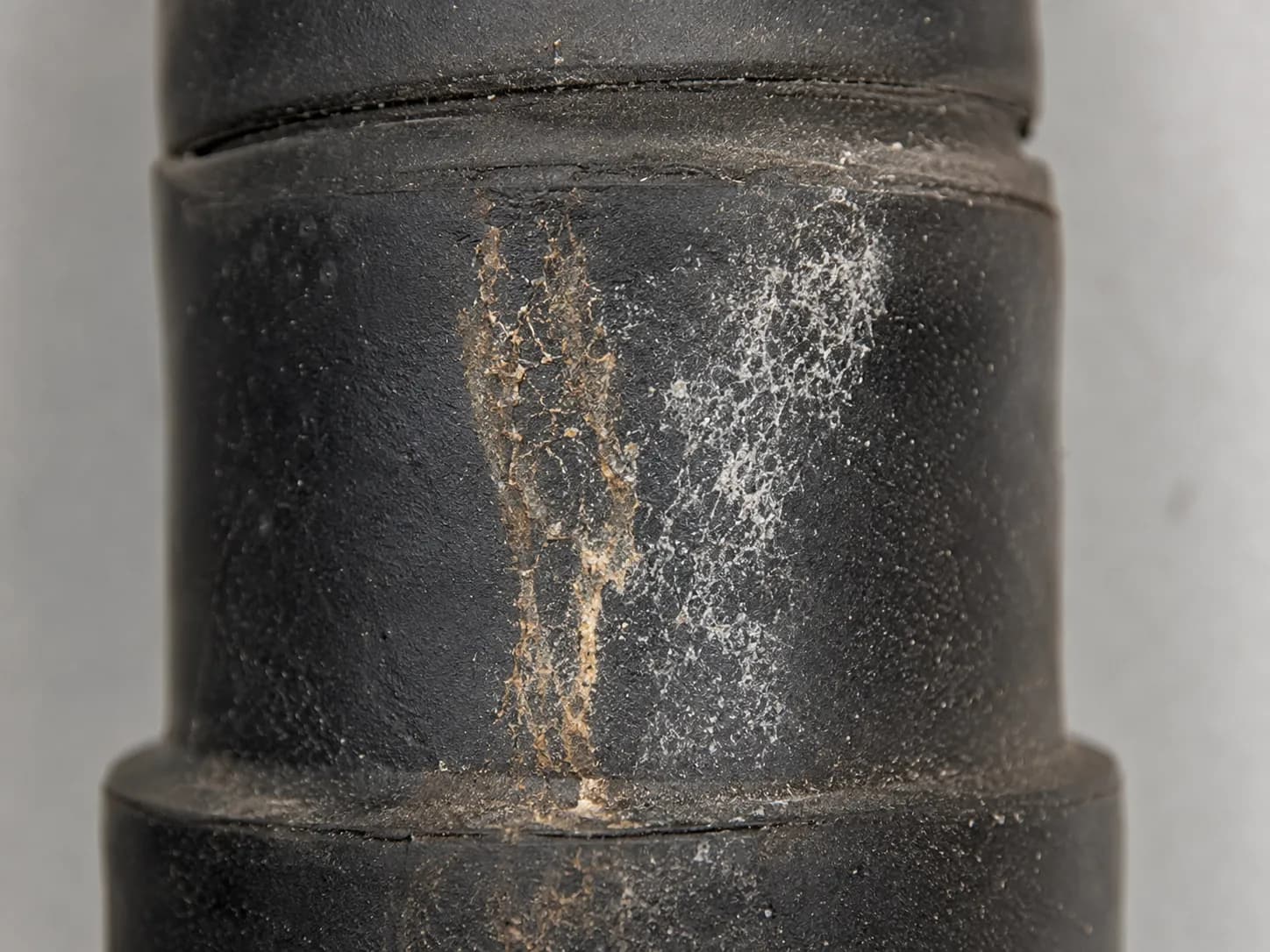 Extreme macro of a black rubber spark plug boot showing brown electrical tracking residue and chalky white deposits on the exterior, indicating high-voltage leakage and insulation breakdown.