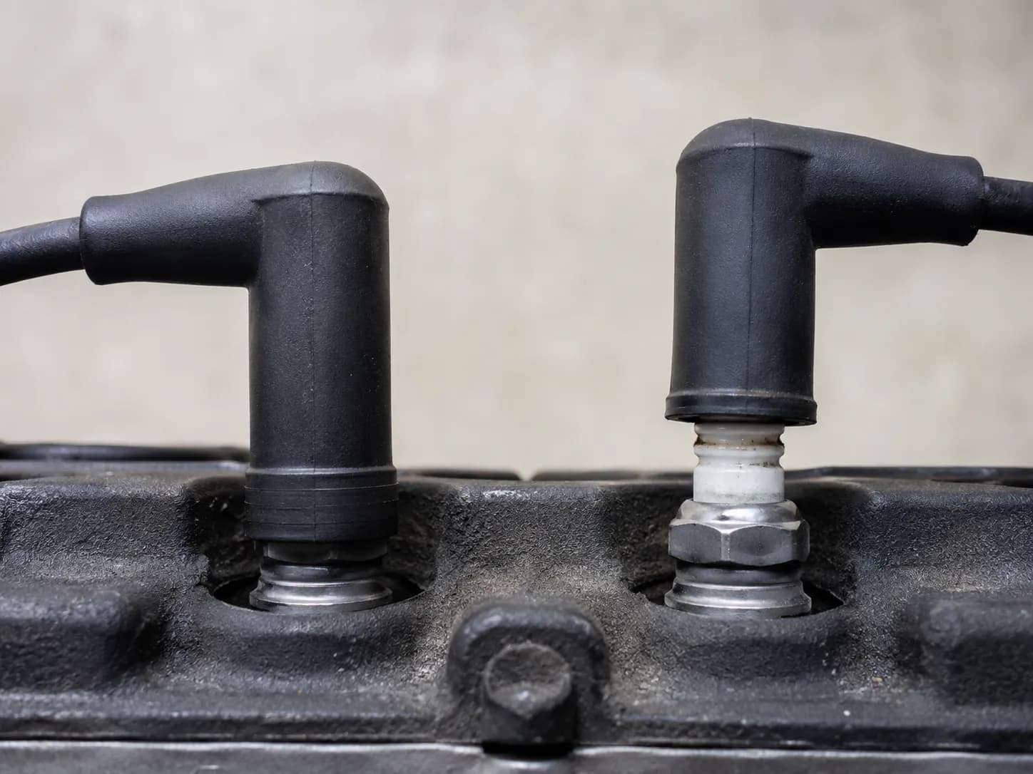Two spark plug boots on engine plugs side by side, one fully seated and one partially lifted to show the correct and incorrect fit on a small engine.