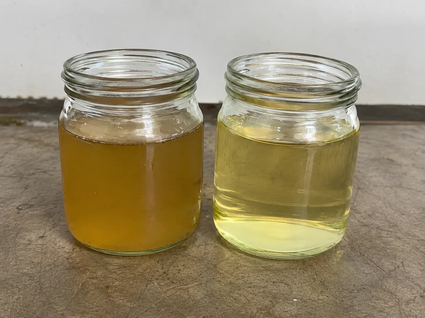 Two clear glass jars comparing cloudy stale gasoline on the left with clean fresh gasoline on the right on a workbench.