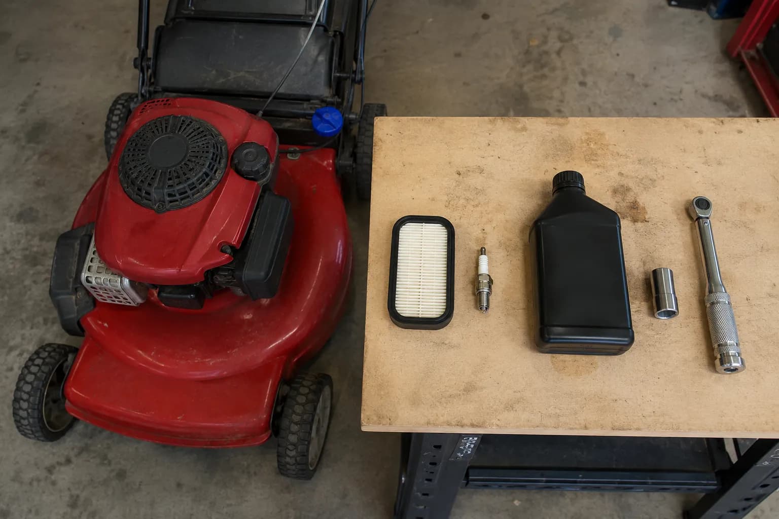 Toro Recycler mower beside a workbench with an air filter, spark plug, SAE 30 oil, socket, and torque wrench ready for service.