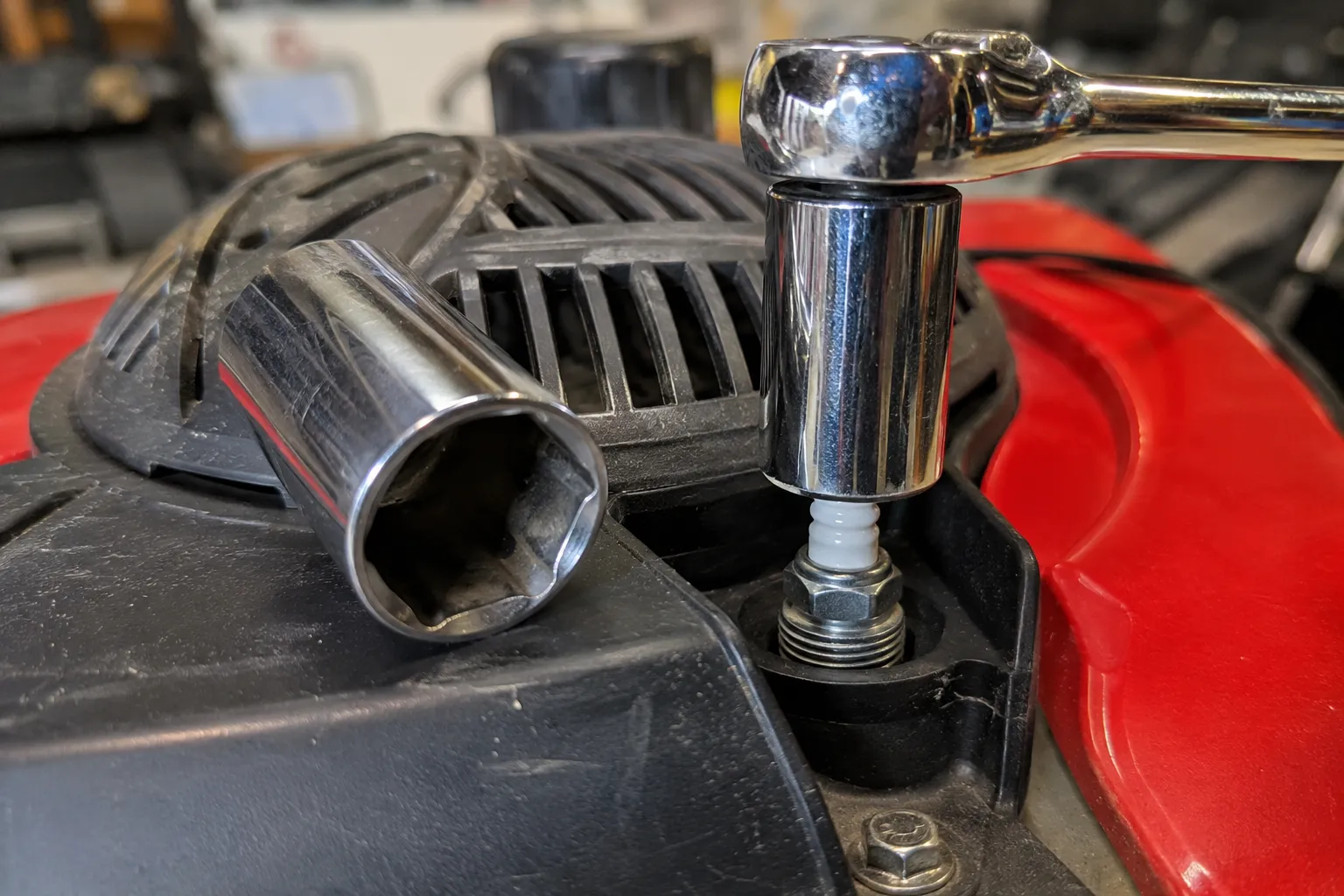A 5/8-inch deep socket fitted onto a Toro lawn mower spark plug with a larger 13/16-inch socket resting beside it for size comparison.