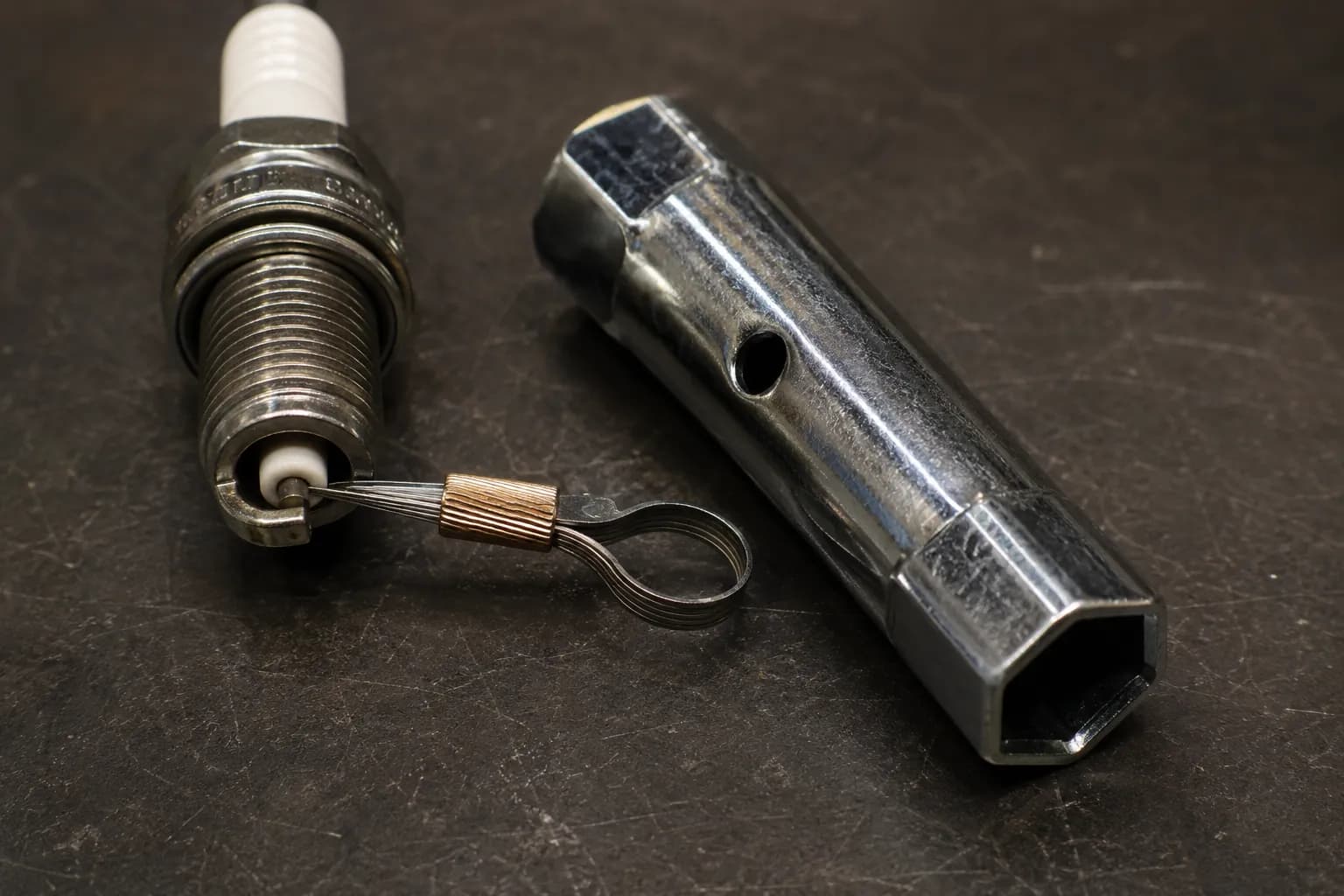 0.030-inch wire feeler gauge checking a spark plug gap beside a Briggs & Stratton 19576S dual-end spark plug wrench showing both hex socket sizes on a workshop bench.