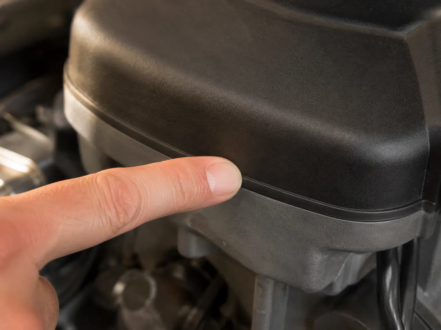 Finger checking the flush seam between a newly installed air cleaner cover and its base on a lawn mower engine to verify a proper airtight seal.
