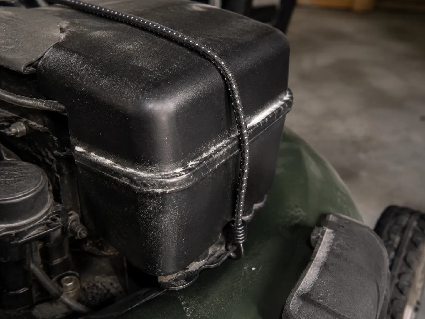 Close-up of an air filter cover secured with a bungee cord, showing talcum powder tracking through a corner gap where the cover does not seal flush during a leak test.