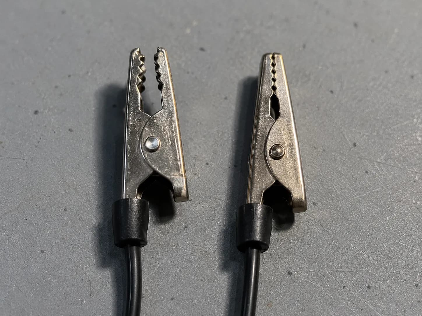 Worn alligator ground clip after 12 clamp cycles beside a new clip, showing reduced spring tension and widened jaws on a spark plug tester lead.