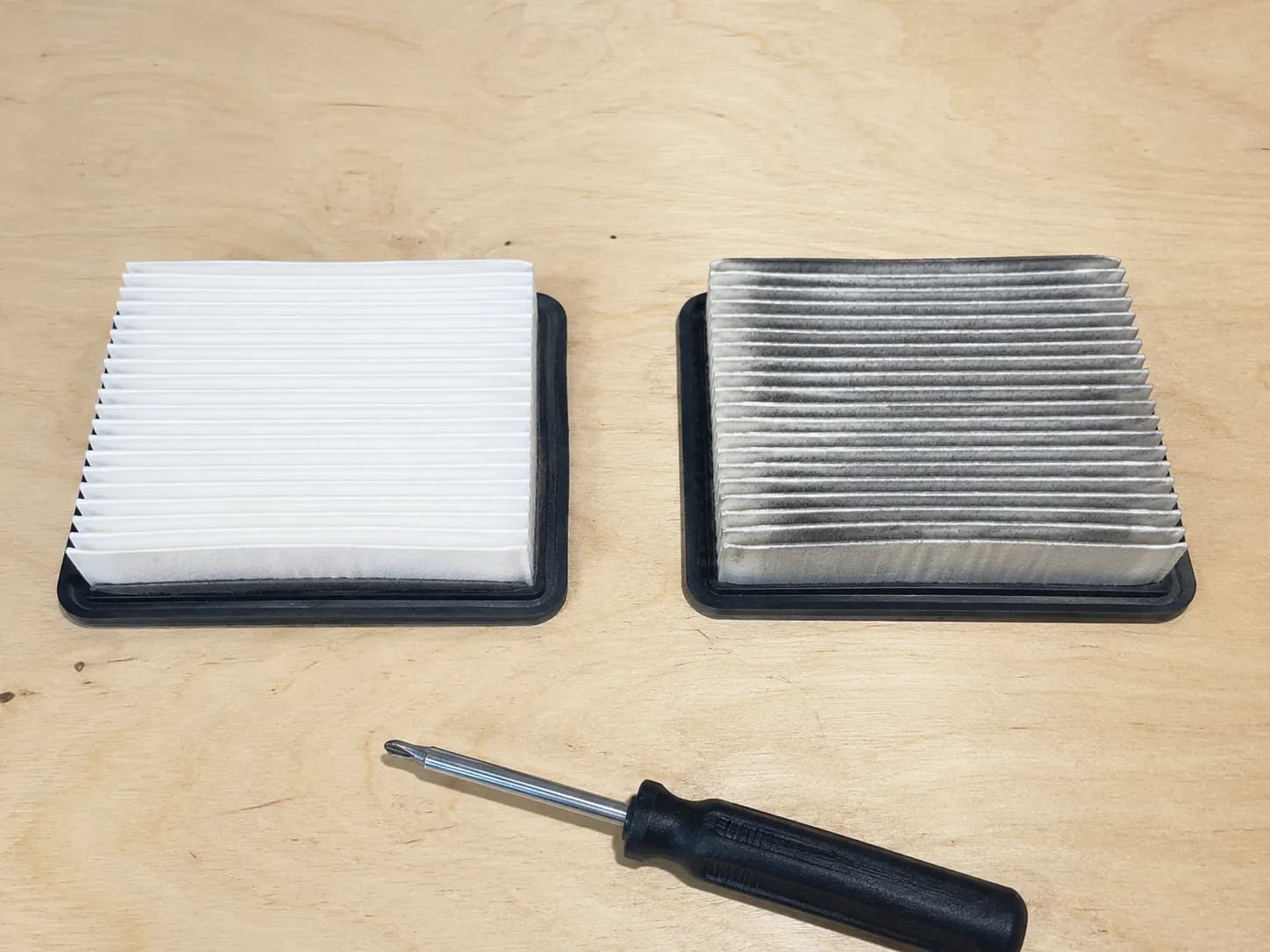 New and used Briggs EX Series style air filters shown side by side on a workbench with a screwdriver, illustrating the difference between a clean replacement filter and a dirty worn filter.
