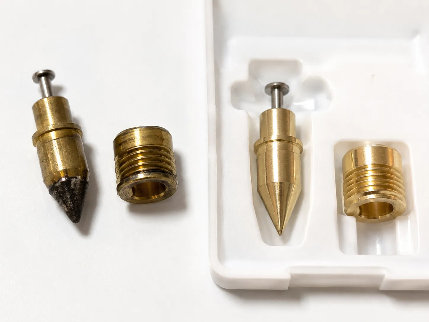 Worn carburetor needle and seat beside new replacement parts, showing varnish buildup and wear before installation during carburetor rebuild.