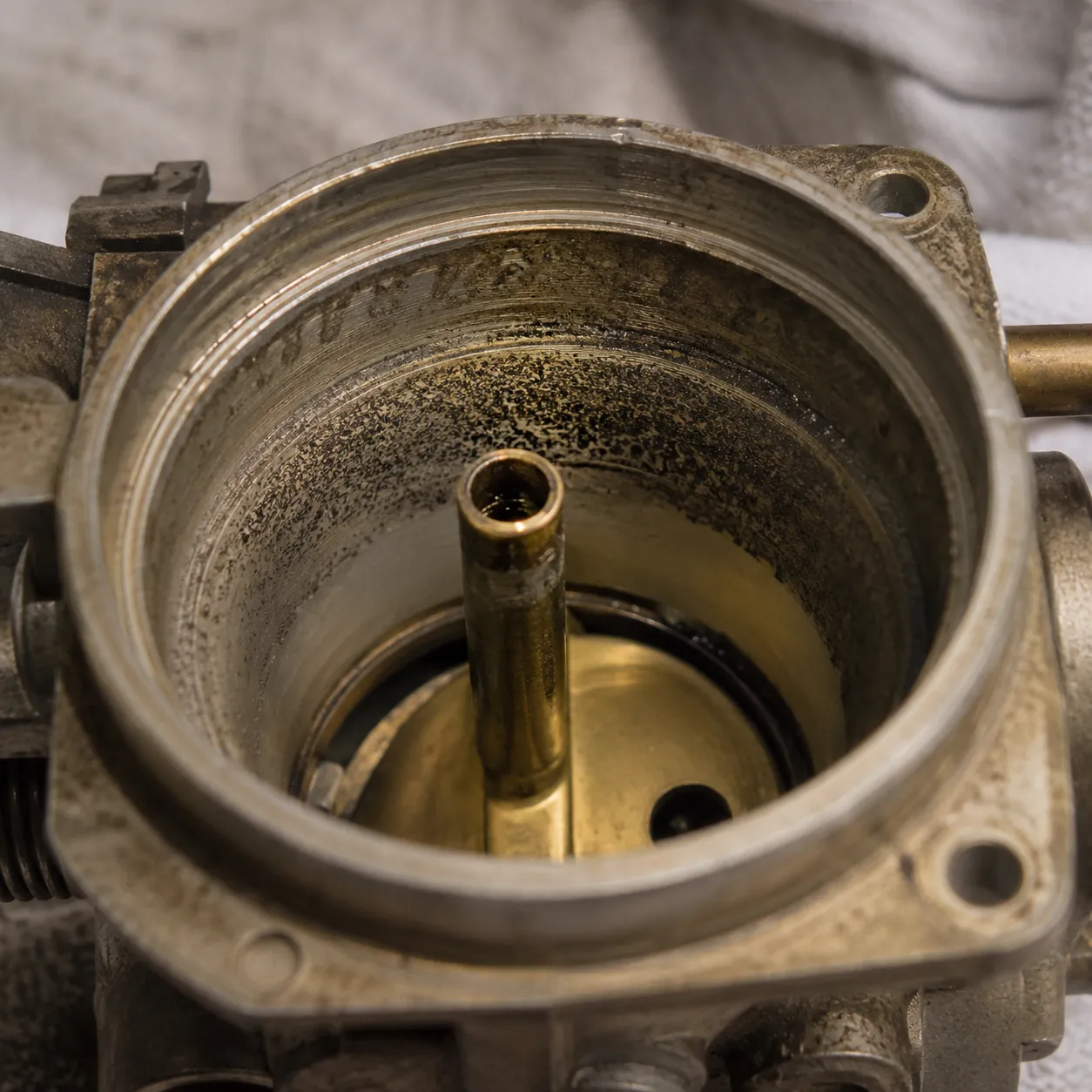 Close-up of a small engine carburetor throat showing a dark band of fine grit contamination around the inner wall from dust entering an uncovered mower.