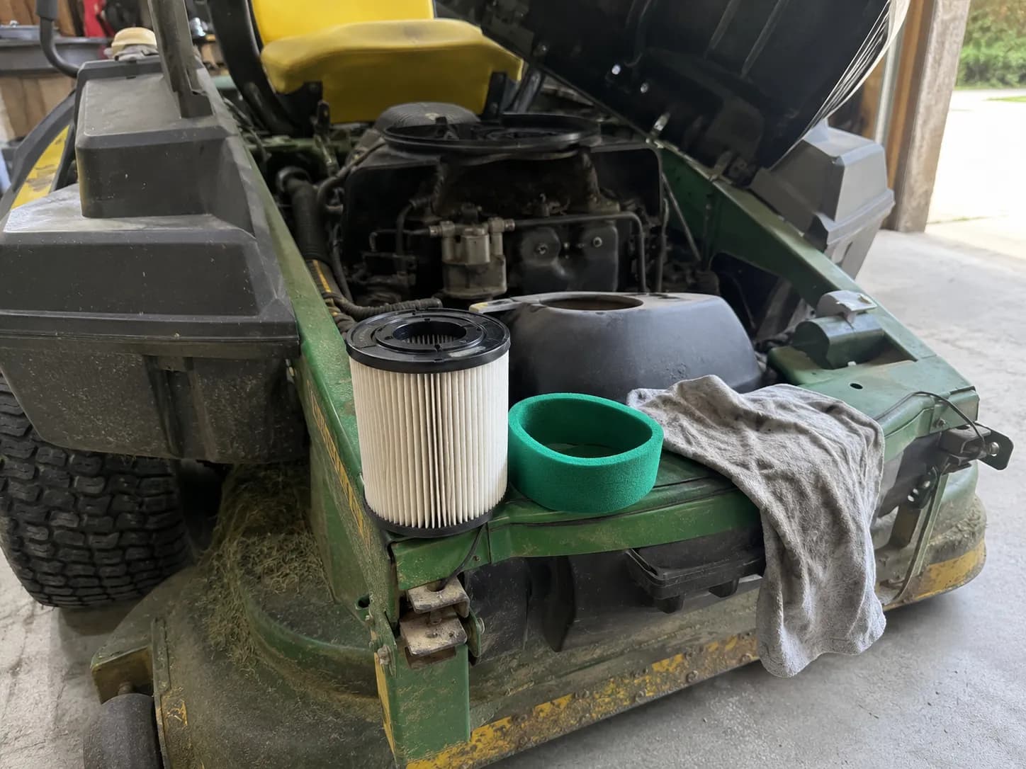 Freshly cleaned paper air filter and green foam pre-filter resting on a zero-turn mower with the engine cover open, showing the air filter was not the cause of the engine running rough.
