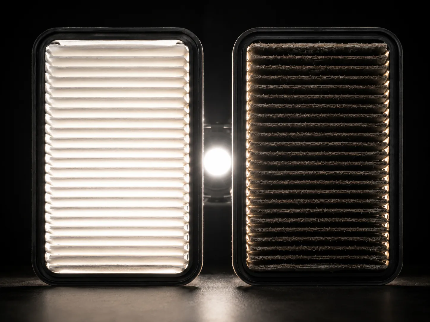 Side-by-side comparison of a clean and clogged lawn mower air filter under the same backlight, showing how a dirty filter blocks airflow while a clean filter lets light pass through.
