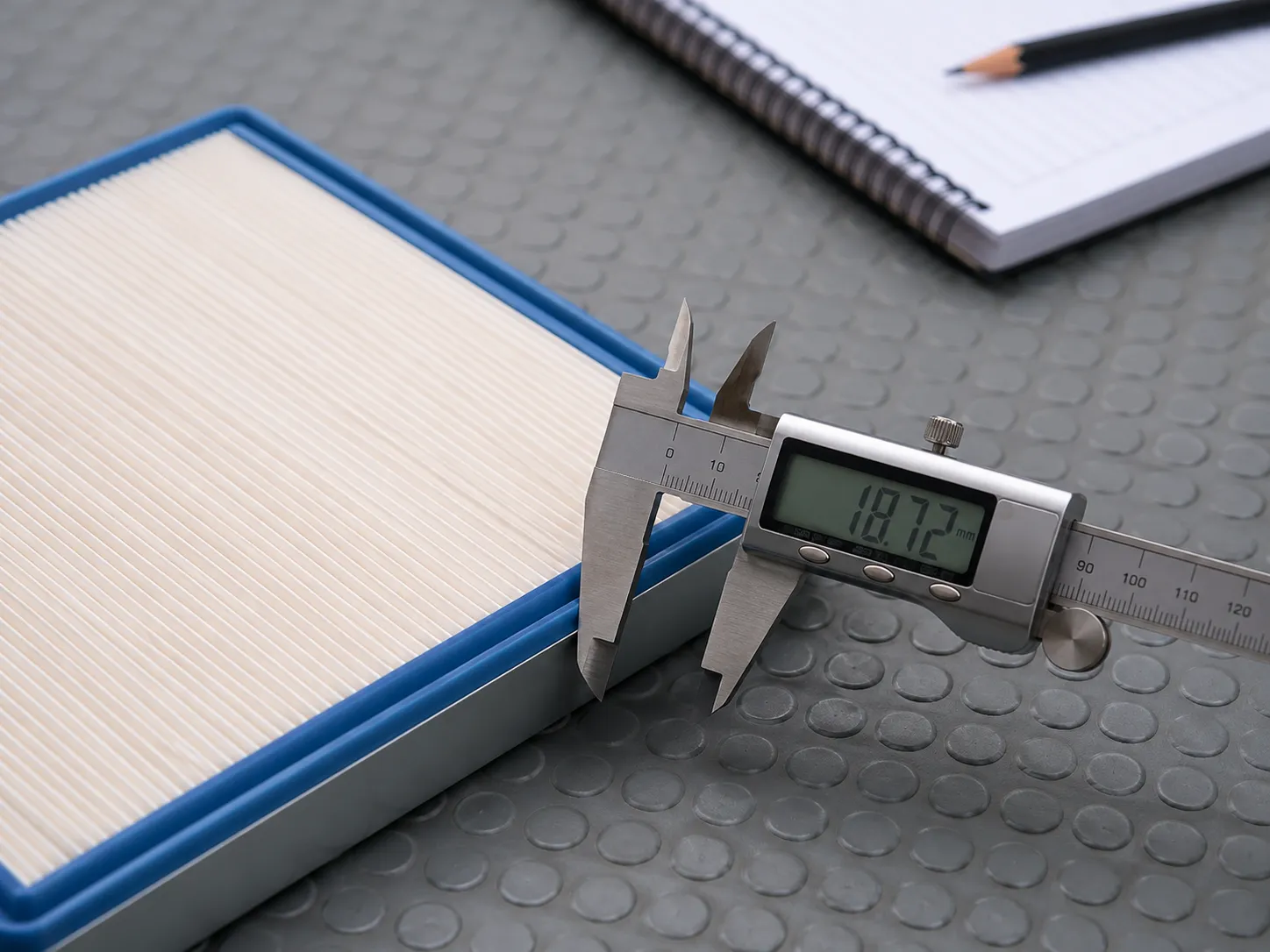 Digital caliper measuring the sealing face thickness of a Honda flat panel air filter on a workshop mat during March–April 2026 reconciliation, with a notepad in the background.