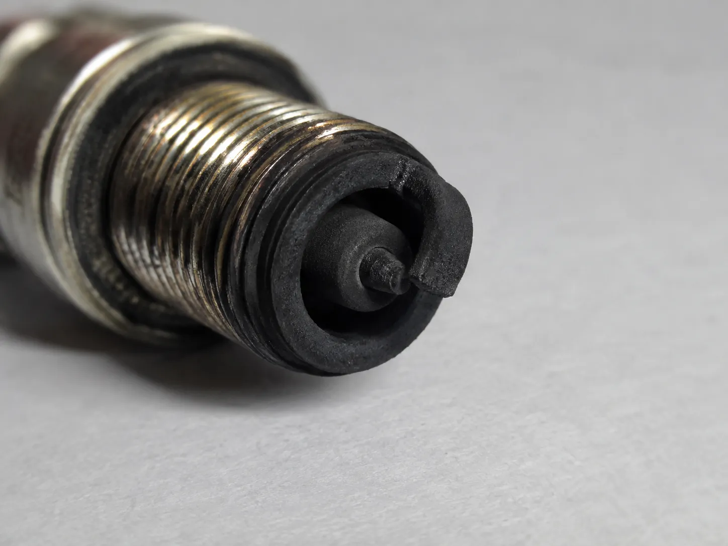 Used spark plug with dry, velvety black soot deposits on the electrode and ceramic insulator, showing a carbon-fouled plug that may indicate an air filter issue.