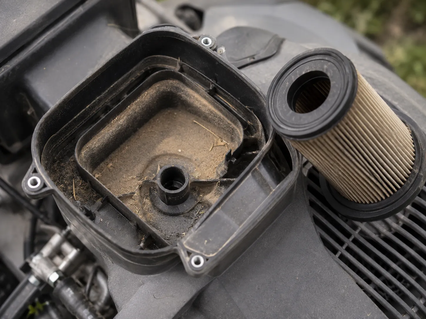 Close-up of a lawn mower air filter housing showing fine dust inside the engine intake track after running with a cartridge filter but no foam pre-cleaner installed.