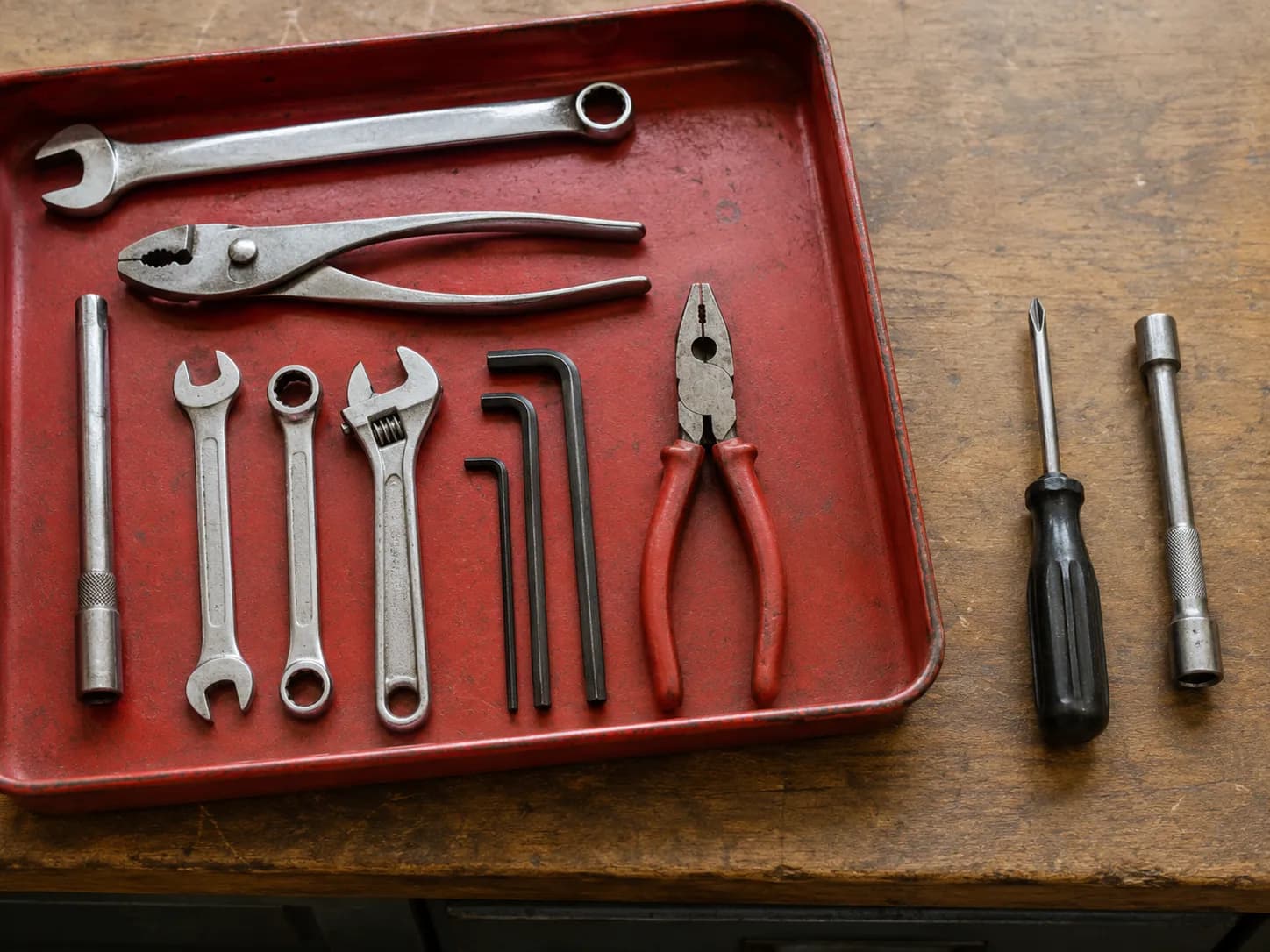 Overhead view of an open red metal tool tray after the final swap on 26 April 2026, with a Phillips screwdriver and 8 mm nut driver set apart beside the untouched remaining hand tools.