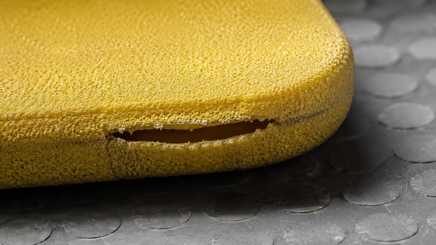 Macro close-up of a lawn mower foam air filter with a split bonded seam, showing hidden damage caused by wringing that can allow unfiltered air into the small engine.