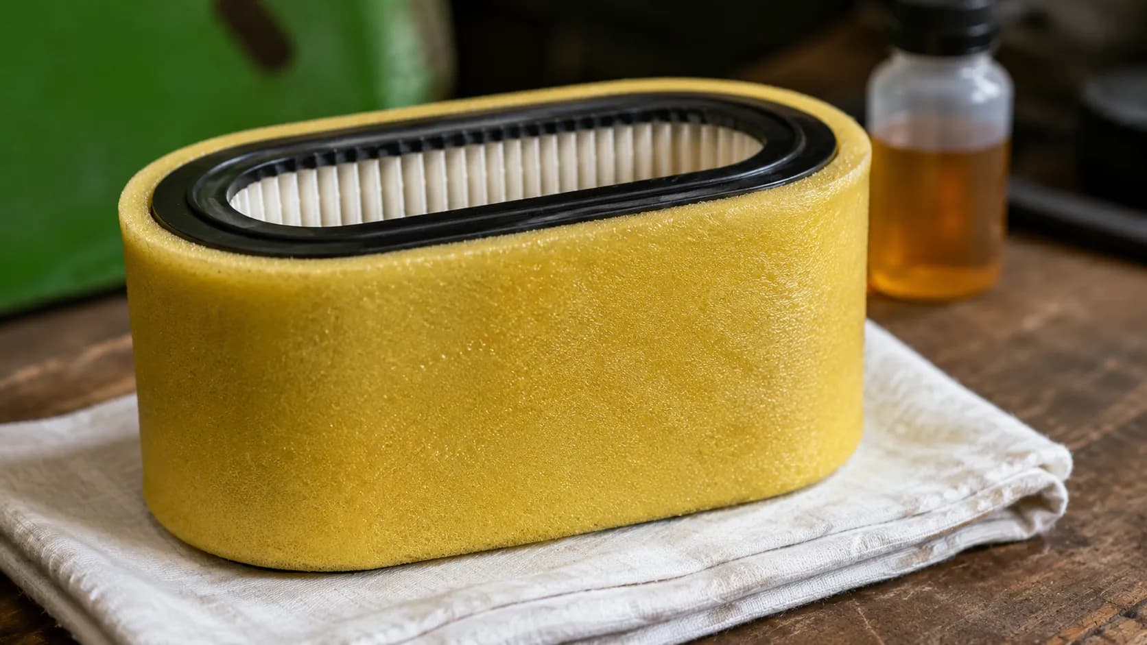 Yellow foam pre-cleaner lightly oiled and wrapped around a white pleated paper air filter cartridge on a workshop bench before installation in a lawn mower engine.