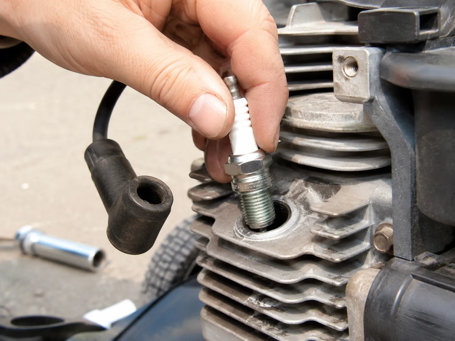 Hand-threading a new spark plug into a Craftsman lawn mower engine cylinder head to prevent cross-threading before tightening with a socket.