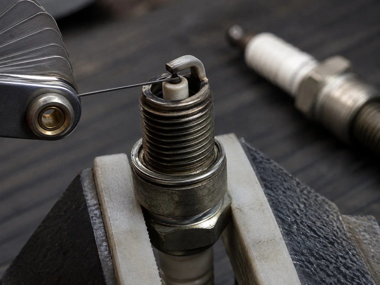Wire gap gauge measuring the as-removed electrode gap on a Honda GCV160 lawn mower spark plug, showing a 0.034-inch gap compared with the recommended 0.030-inch specification.