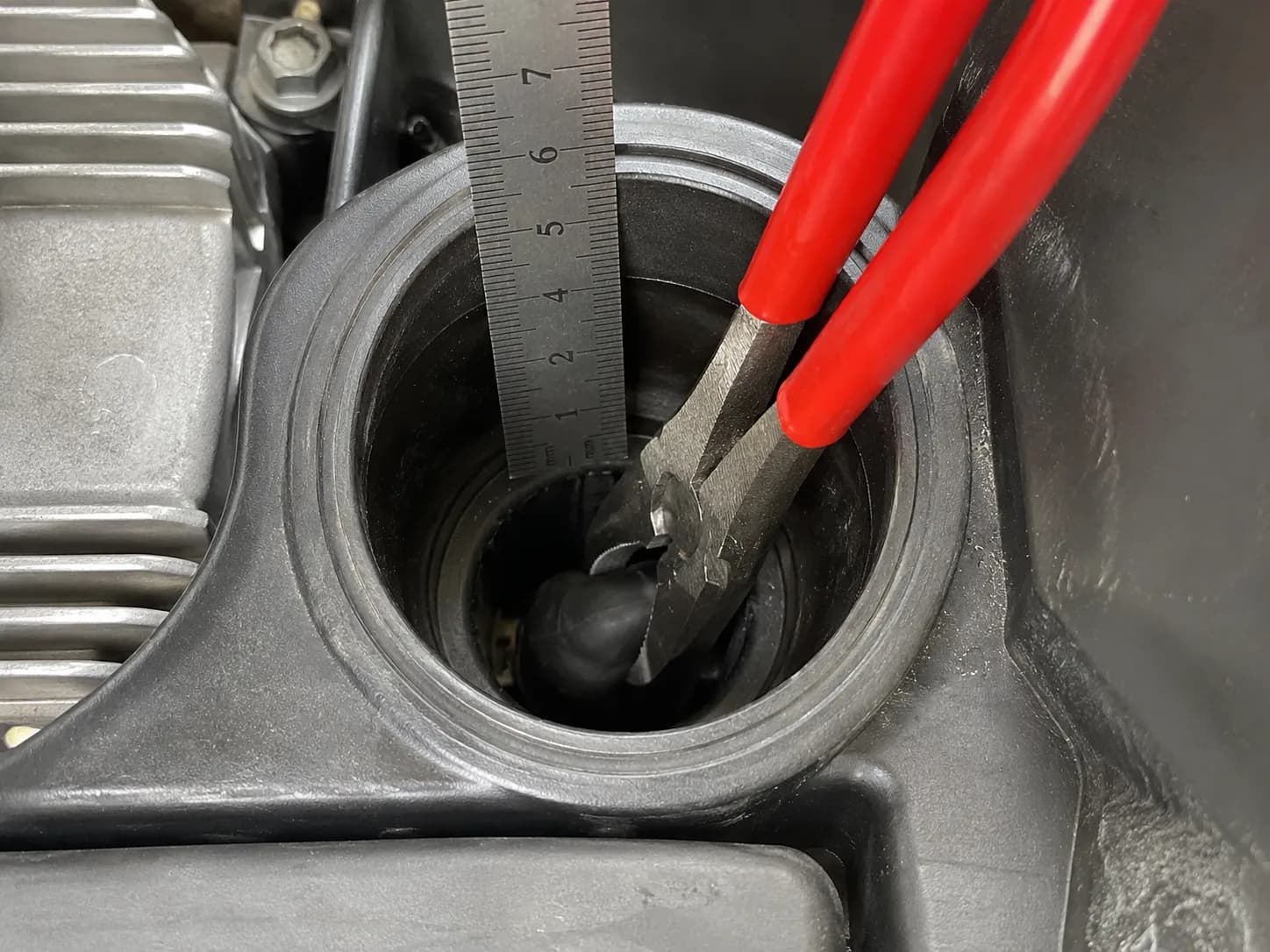 Insulated pliers gripping the spark plug boot inside the recessed spark plug well of a Honda GCV170 engine, with a steel ruler showing recess depth.
