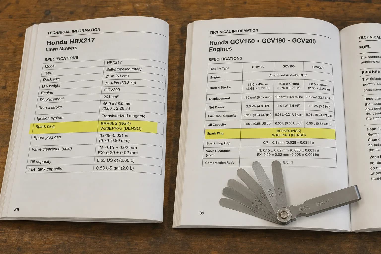 Two Honda equipment manuals opened side by side on a wooden bench, highlighting different recommended spark plugs, with a feeler gauge resting in one corner for comparison.