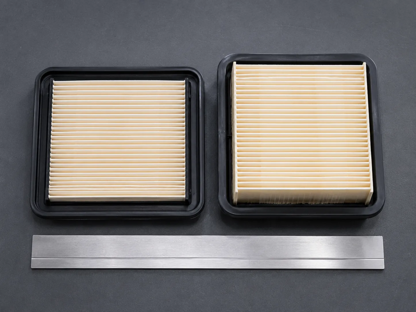 Two rectangular Honda lawn mower paper air filters side by side, showing the newer deeper filter beside the older shallower element with a steel ruler for size comparison.