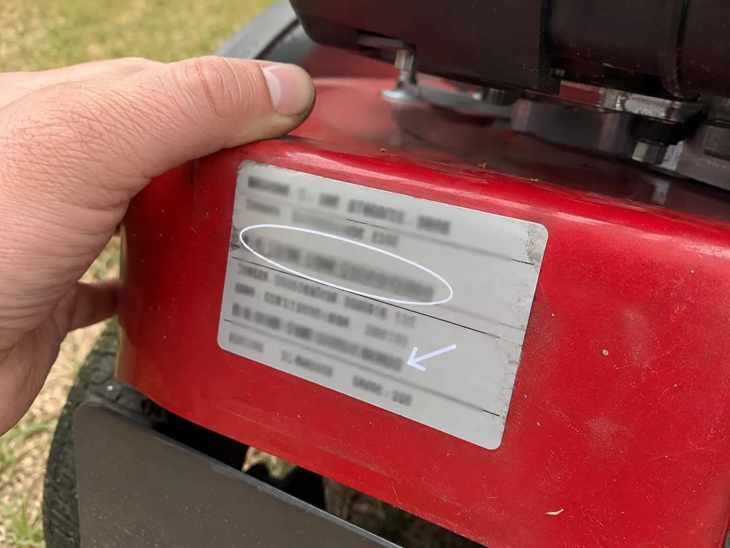 Close-up of an HRR216 mower deck identification sticker with the serial line circled and an arrow pointing to the engine model line, showing where to find matching identification details.