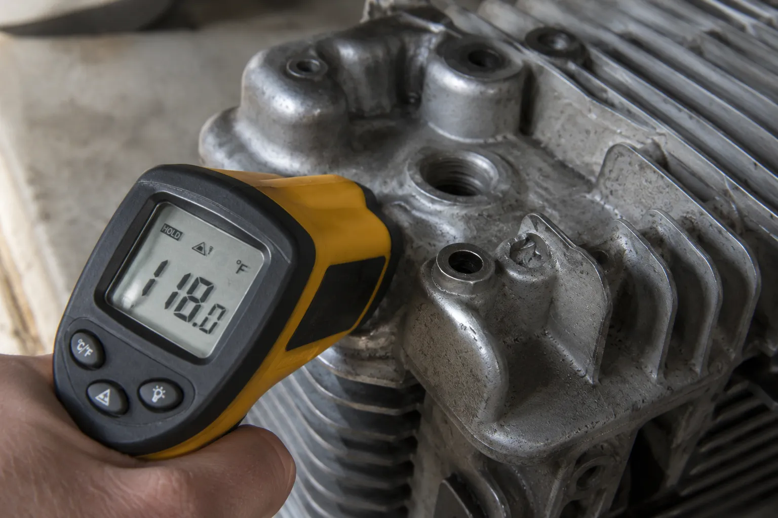 Infrared thermometer measuring 118°F at the spark plug boss on an aluminum small engine cylinder head before attempting stuck spark plug removal with controlled heat.