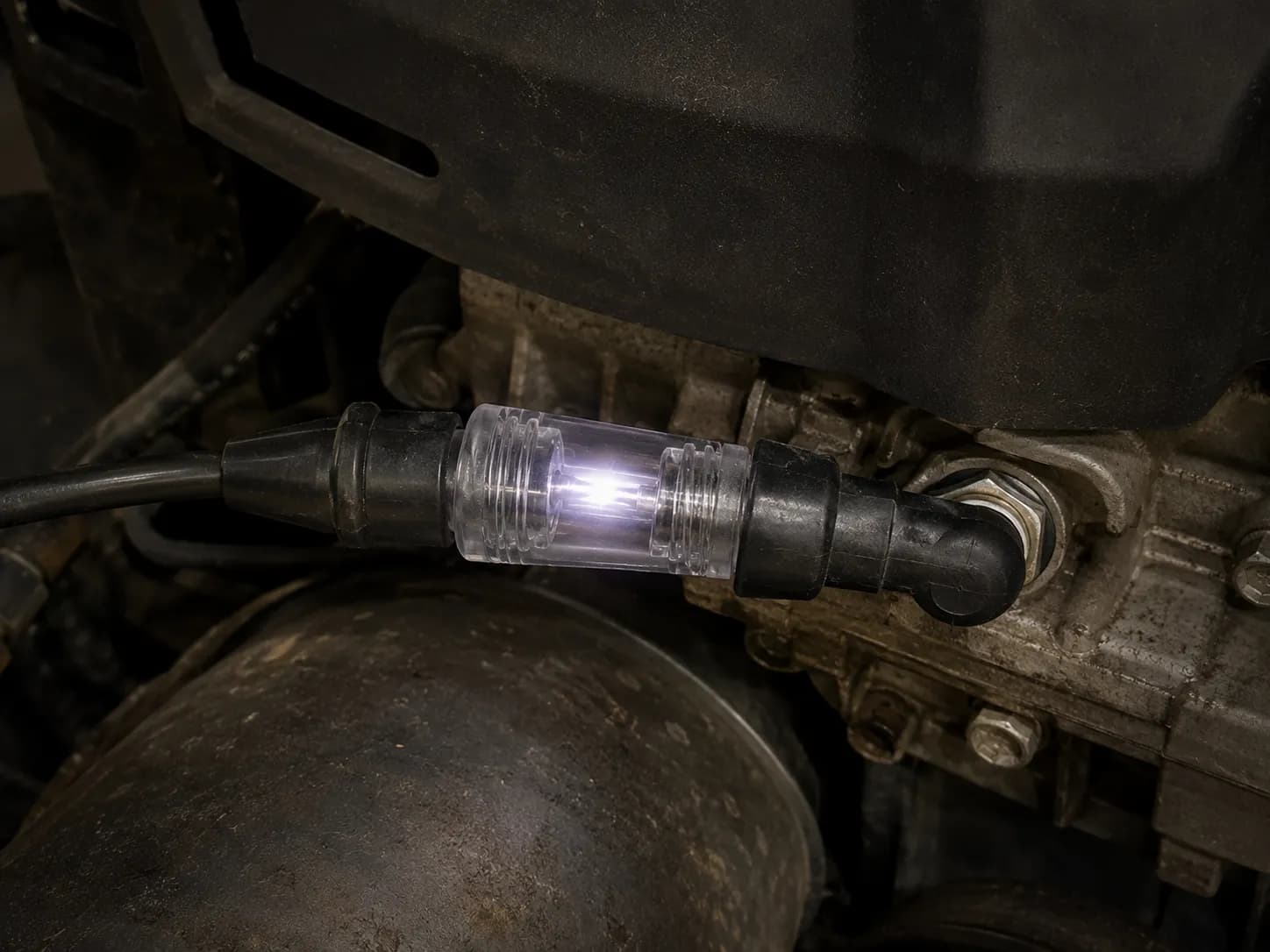 Inline spark tester connected between the ignition lead and installed lawn mower spark plug, showing a bright flash in the tester window to confirm the ignition system is producing spark.