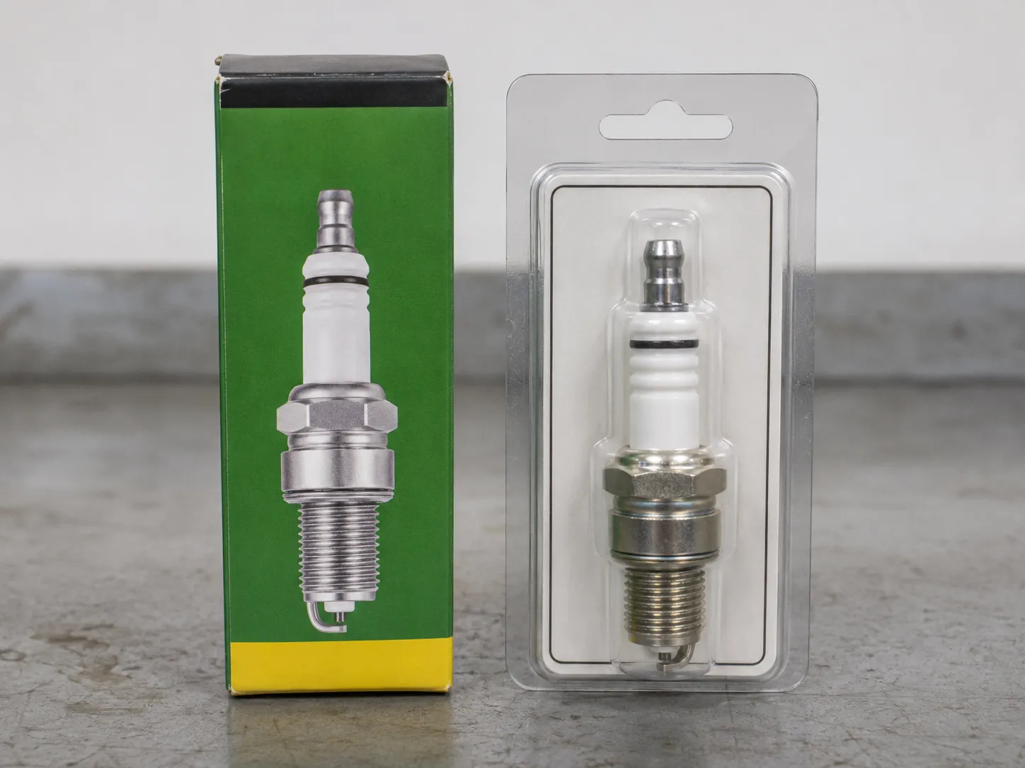 John Deere M78543 spark plug box beside an identical Champion RC12YC spark plug in a clear blister pack on a gray workbench, shown for packaging comparison.