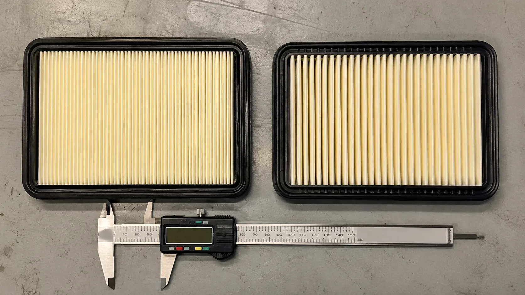 Side-by-side comparison of a genuine OEM and quality aftermarket flat riding mower air filter showing different pleat density with digital calipers on a workshop bench.