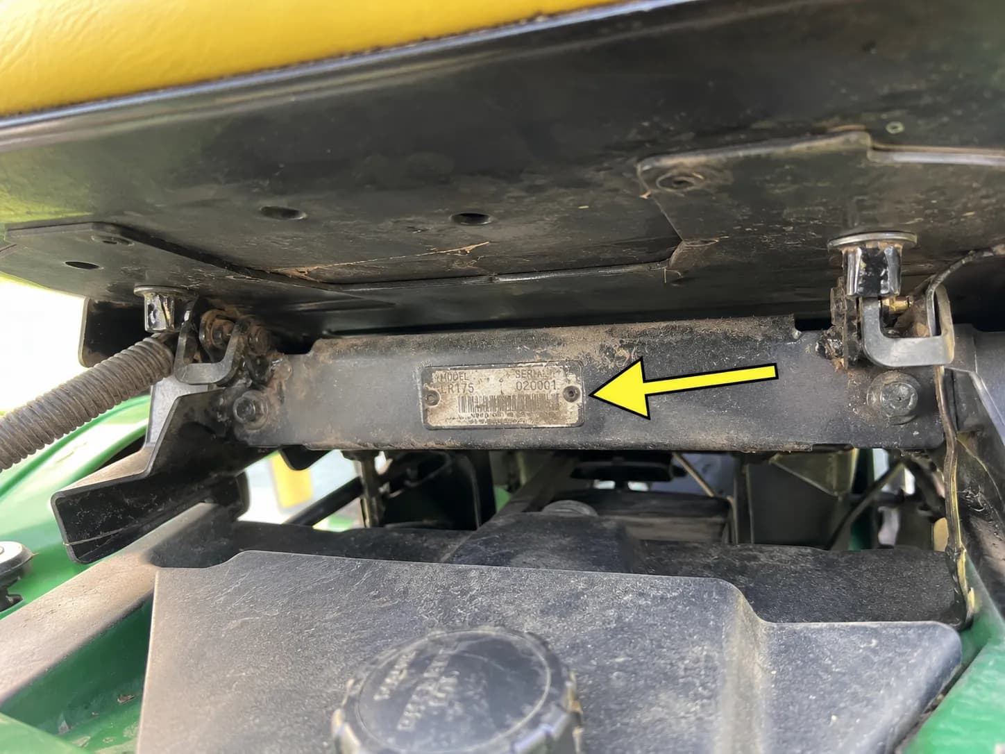 Close-up of a John Deere riding mower model and serial identification plate under the seat, highlighted with an arrow.