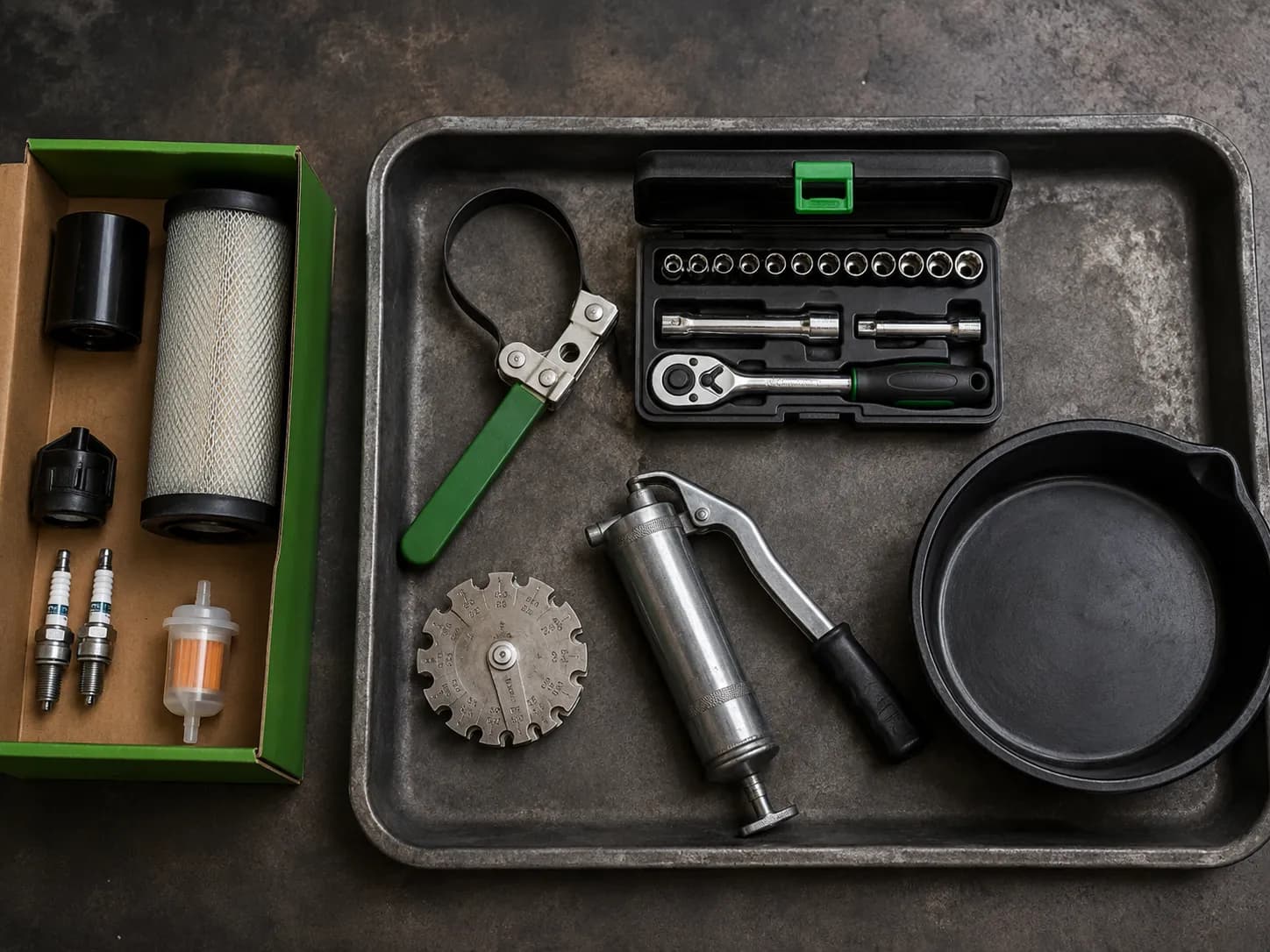 Overhead view of John Deere riding mower tune-up tools including an oil filter wrench, socket set, spark plug gap gauge, grease gun, drain pan, and an opened maintenance kit arranged on a workbench.