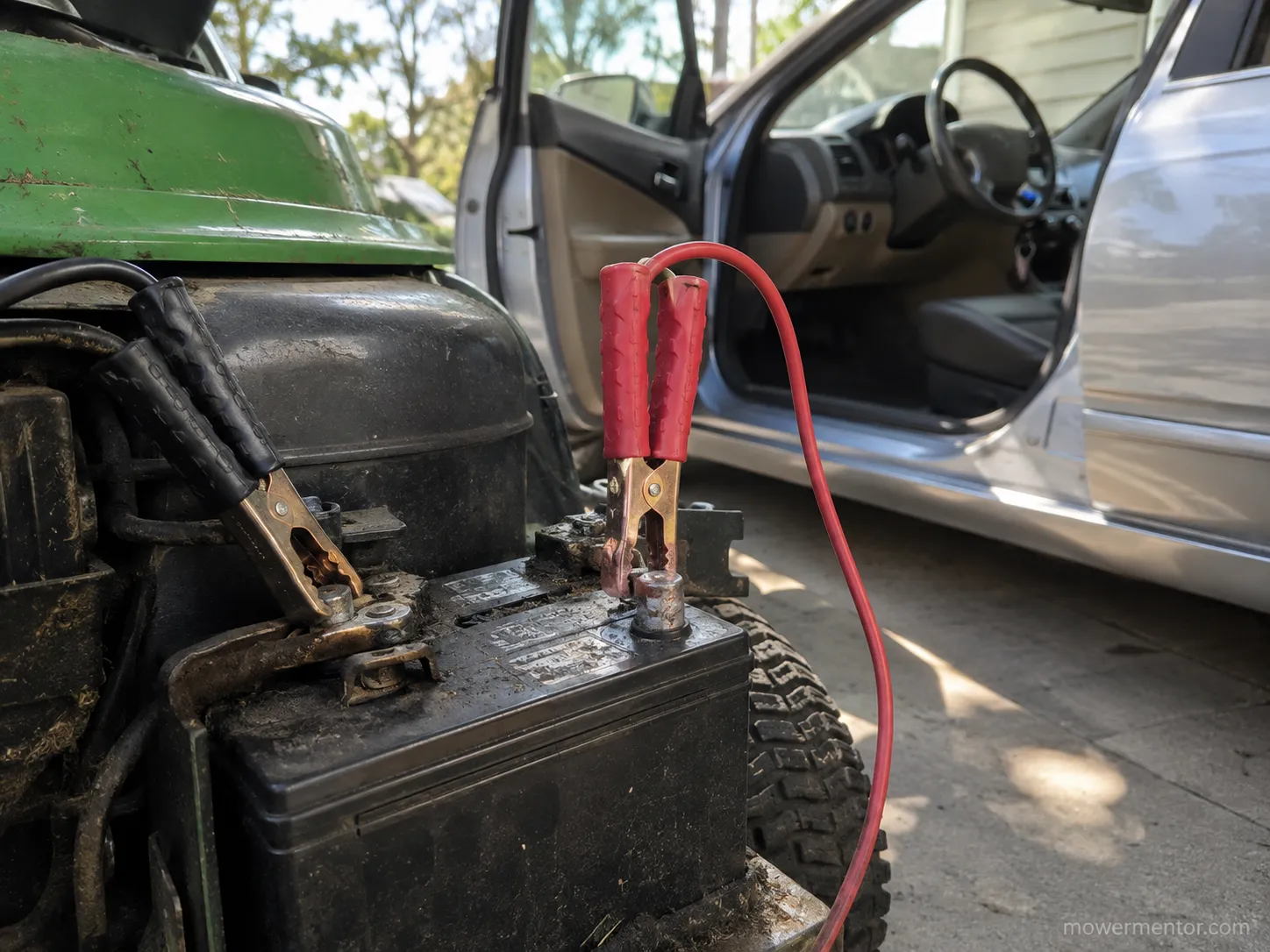 Jumper cables connected to a riding mower battery with the donor car engine off in the background.
