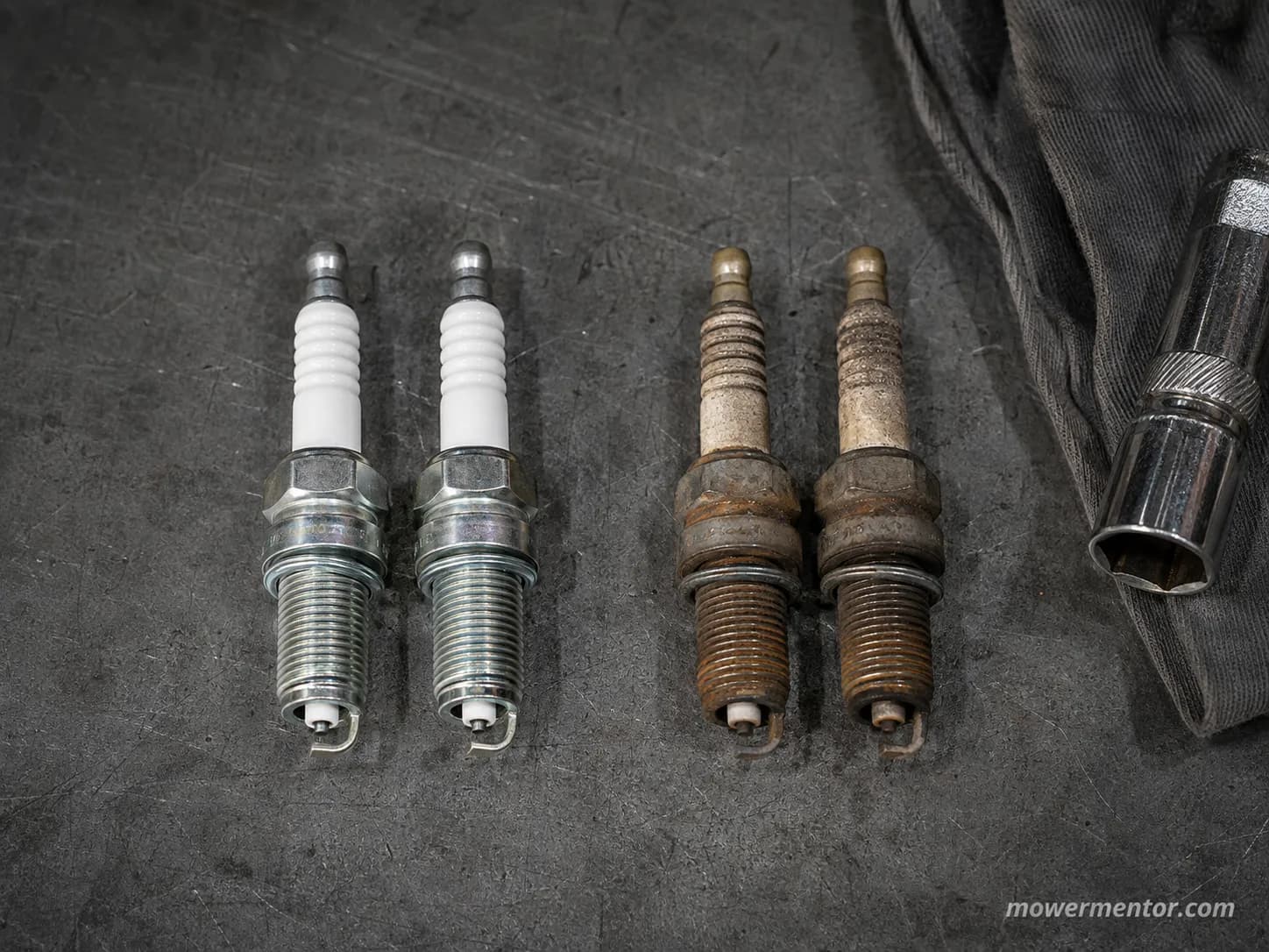 Kawasaki FR691V spark plugs compared new versus 288 hours, showing clean ceramic insulators and worn, carbon-coated electrodes on a workshop bench.