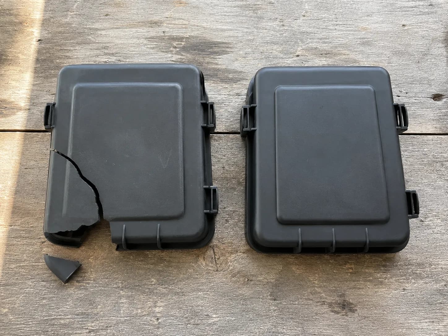 Cracked and intact lawn mower air filter covers shown side by side on a weathered wooden workbench, highlighting that the plastic cover is a separate replacement part prone to cracking.